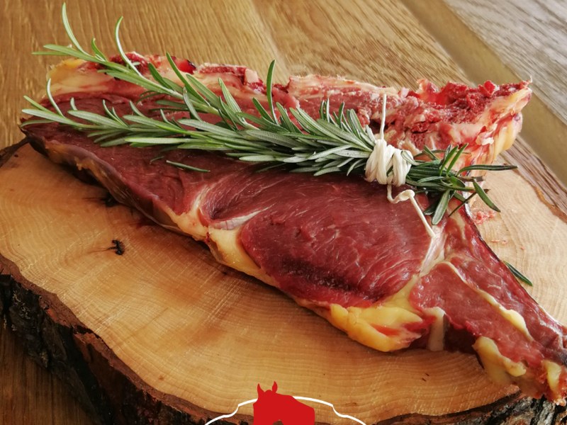 Bistecca cruda di cavallo con osso e rosmarino legato con spago su fetta di tronco, logo Taberna Equina