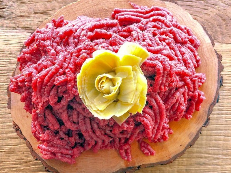 Pesto di cavallo Taberna Equina su un tagliere di tronco, guarnito al centro con un carciofo aperto a forma di rosa